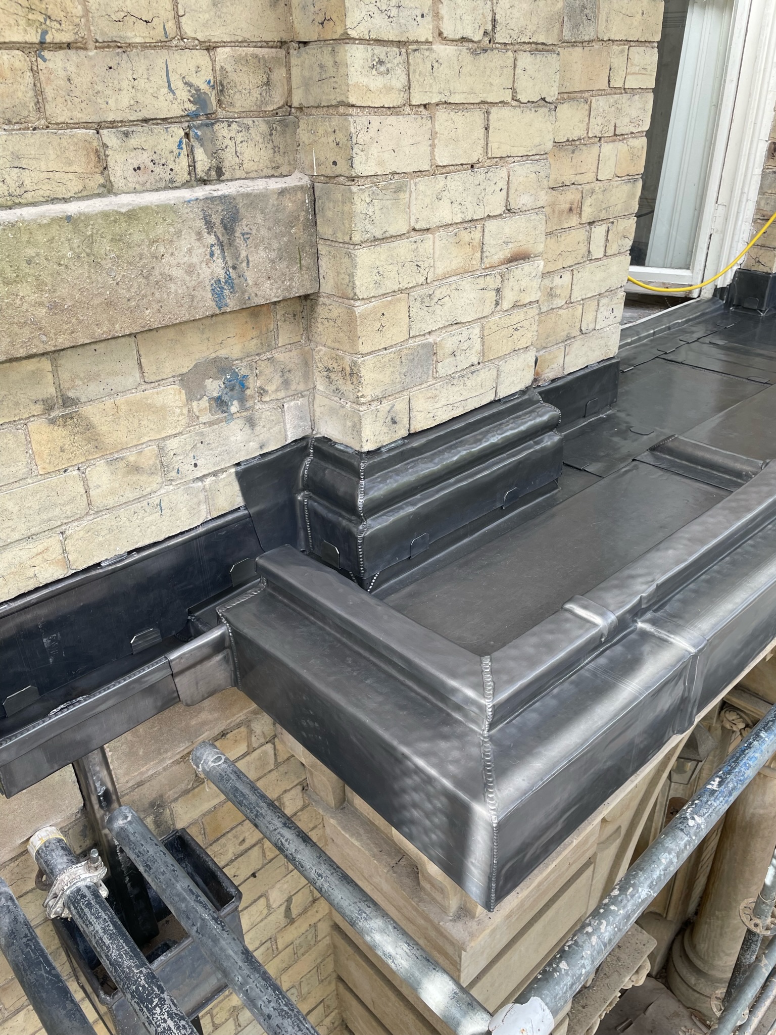 Lead flashing detail covering a curved decorative stone plinth with a raised upstand