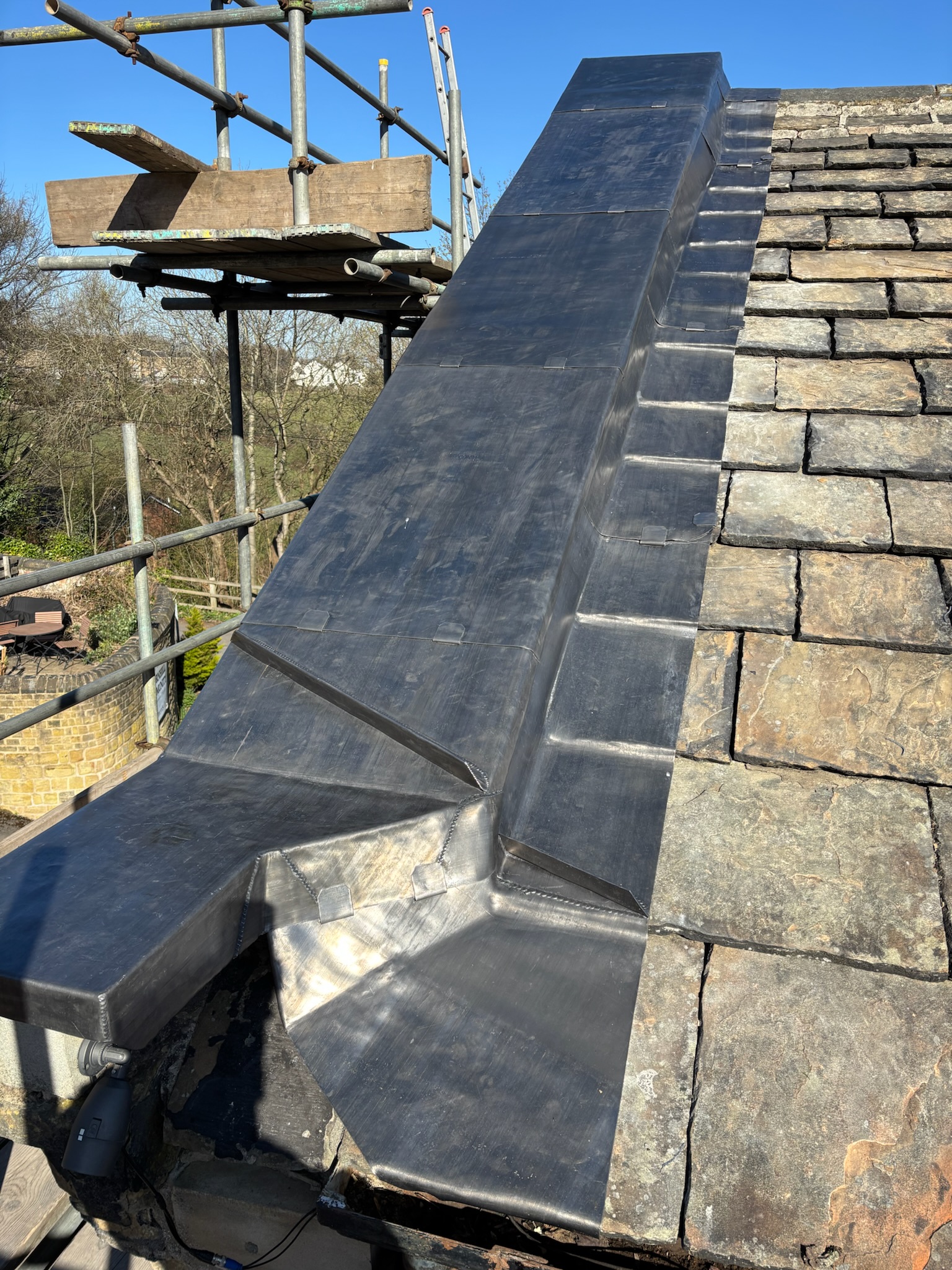 Lead cover flashing detail onto a stone slate roof over a stone coping